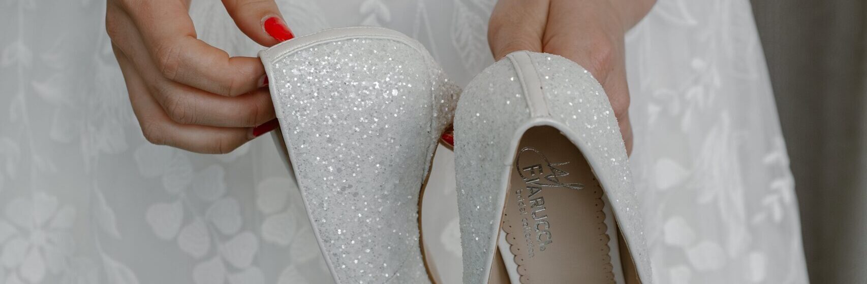 a person holding up a pair of white weddingshoes