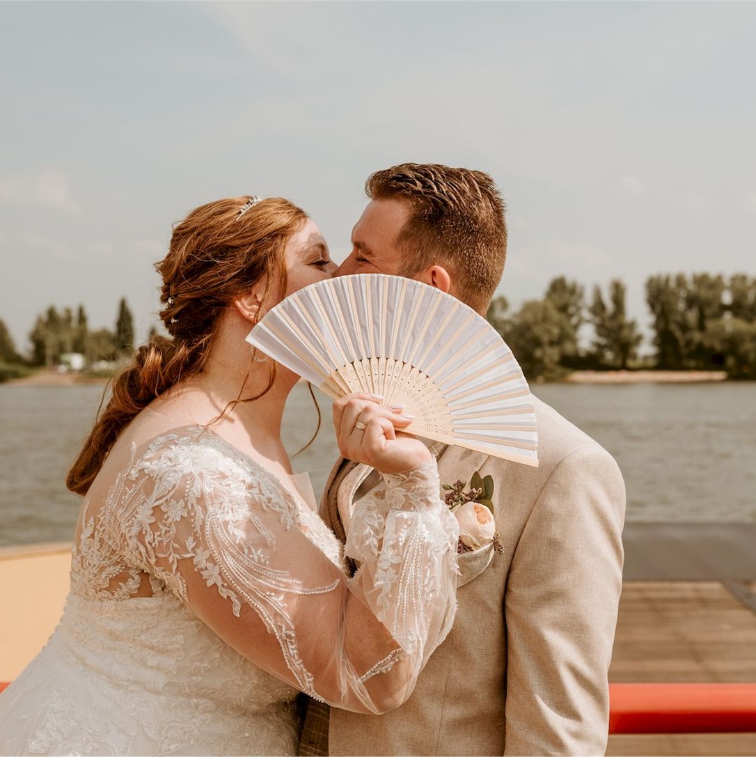 Een bruid en bruidegom kussend achter een waaier, foto gemaakt door Foto Mariek